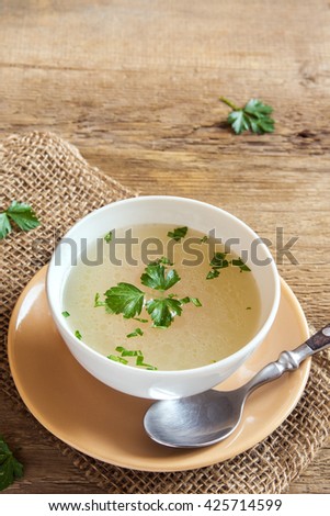 Chicken broth with parsley in white bowl over wooden background with copy space