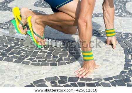 Brazilian athlete wearing flip flops crouching at the start position in running blocks on the tiles of the Ipanema boardwalk in Rio de Janeiro, Brazil