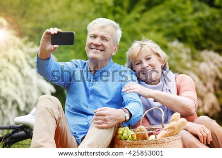 Portrait of happy senior couple taking selfies with smart phone while picnic and relaxing outdoor.