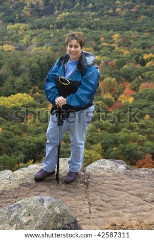 Adult female hiker standing at the edge of a  cliff high above forest