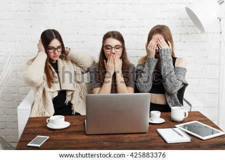 Three young women with computer showing blind, deaf: three wise monkey scene - hear no evil, see no evil, speak no evil. Girls look at monitor show indifference, negation, silence.