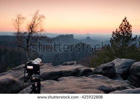 Tripod with big camera stand on mountain peak after sunset. Sharp sandstone cliffs at horizon