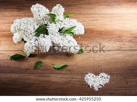 Still life. Bouquet of white lilacs in white a vase on a 
wooden table ,Heart with petals.