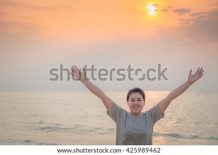 Happy Asian young woman standing with her arms raised to her head enjoy on the beach. Sunset in the background. Summer vacation concept, Thailand