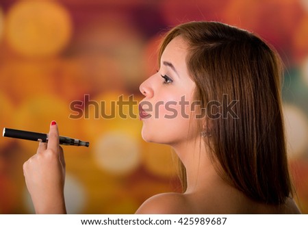 Side photo of woman holding with two fingers a black electronic cigarette, colored background