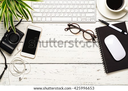Workspace desk with keyboard, smart phone, camera, earphone, eyeglasses, notebook, pen, mouse, cup of coffee and tree, Office table with essentials working stuff