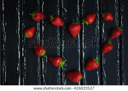 Fresh juicy red strawberries with green tails, lined in a heart shape on a black tree. Photos can be used as an illustration, space for text, card, wedding invitation, background, texture, birthday