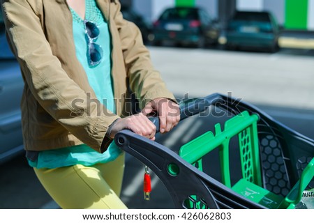 Young woman holding shopping push cart closeup picture of hands with car on background