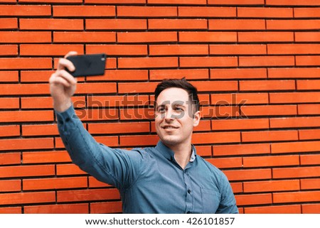 Young adult taking a selfie in front of a brick wall.