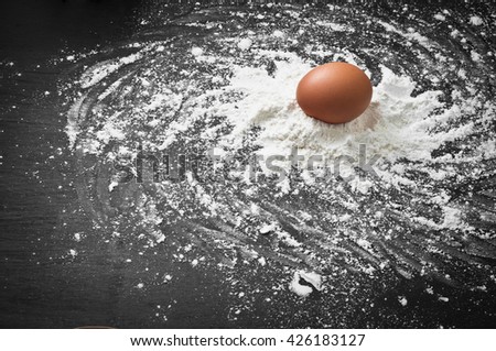 Egg with flour on dark board.