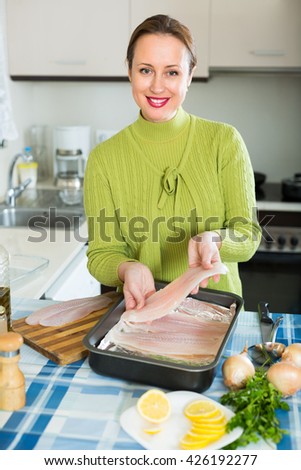 Positive smiling woman cooking filleted fish at home kitchen