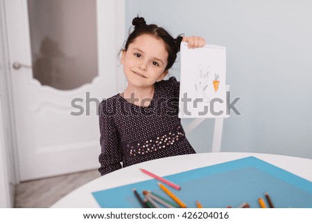 Little beautiful girl draws pencil on a table in the kitchen.