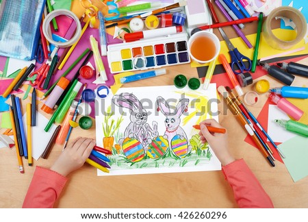 rabbit family on meadow with eggs, easter holiday concept, child drawing, top view hands with pencil painting picture on paper, artwork workplace