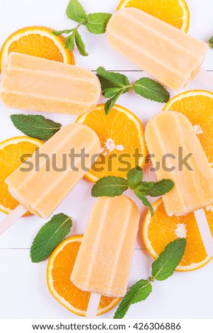 Homemade orange popsicles with mint and orange slices on a white wooden background