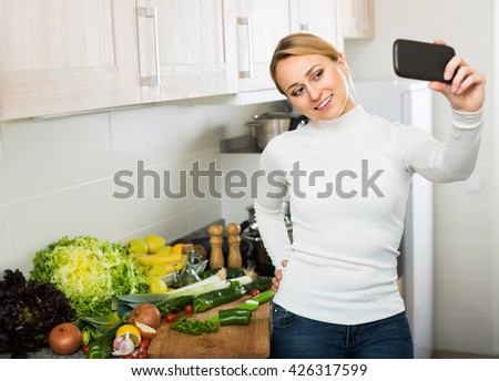 Young happy woman taking selfie with mobile phone at home kitchen
