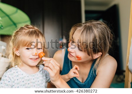 Happy mother and toddler girl painting with ice cubes and paints. They paint their faces and on the paper having fun.