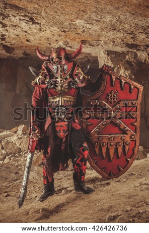 Powerful knight in heavy armor with the sword and shield on the dungeon background.