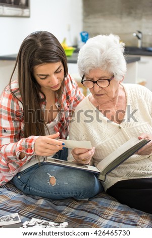 Granny sitting on couch next to her granddaughter and looking through photo album.