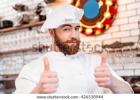 Smiling attractive chef cook showing thumbs up on the kitchen