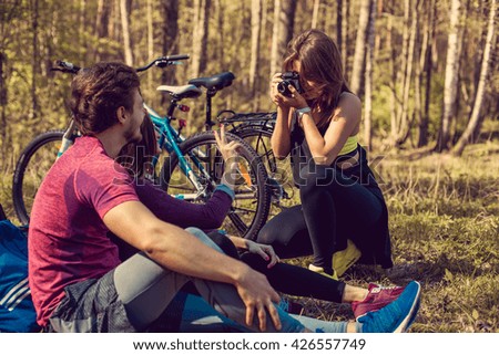 Female photographer shooting sporty couple after bicycle riding in summer forest.