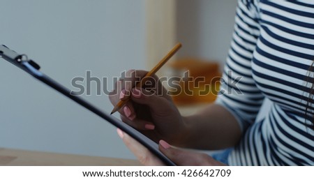Close-up of businesswoman holding pencil in hands and writing a note at office notepad