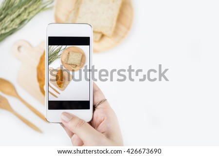 Top view of a female hand taking picture of baked goods with a smartphone, focuses on the hand holding the phone with copy space