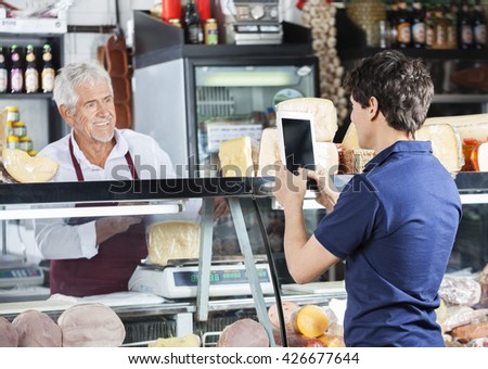 Man Photographing Salesman Packing Cheese In Shop