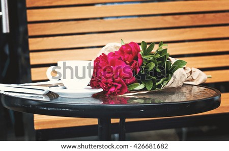 cup of coffee and a bouquet of peonies, bouquet of flowers and a newspaper on the table in a cafe