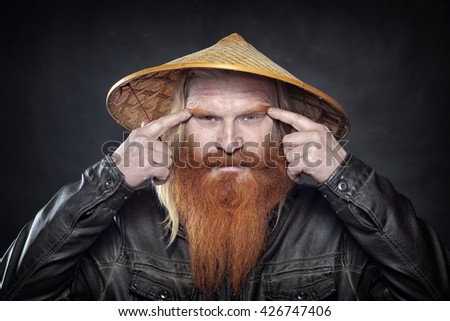 Portrait of an adult man with a red beard and mustache in the Vietnamese hat on a dark background studio
