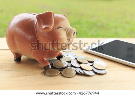 piggy bank -Thai money, tablet computer on wood table, over light [blur and selective focus background]