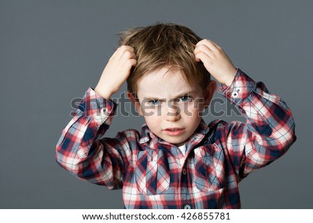 annoyed young boy with freckles scratching his hair for head lice or allergies, grey background studio
