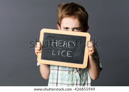 displeased preschool child hiding himself behind a school slate with 'poux' written in French to scare and fight against school head lice, grey background studio