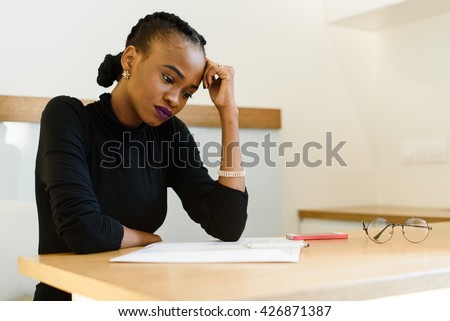Thoughtful worried African or black American woman holding her forehead with hand looking at notepad in office Royalty-Free Stock Photo #426871387