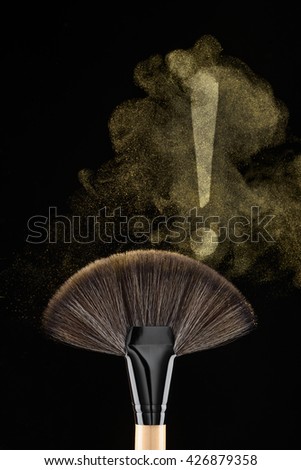 Brush with the mark of exclamation made of golden elements of cosmetics in the air. Luxurious color of qualitative cosmetics. Vertical minimalistic shot.