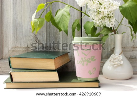Composition with pile of vintage books with green cover, porcelain vase with bouquet of  lilac and paper  coffee