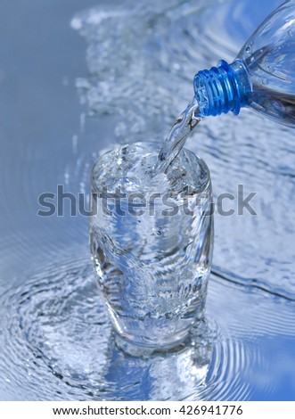 Water flowing from plastic bottle into glass Cup on the background of blue sky