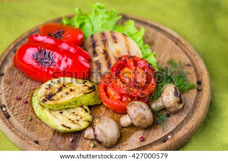 Grilled vegetables - pepper, tomatoes , zucchini , onions and mushrooms on a wooden board . Close-up on a green background.