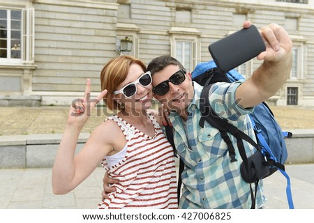young attractive American couple enjoying holiday trip in Spain taking selfie photo self portrait with mobile phone smiling happy having fun wearing traveler clothes carrying backpack