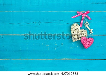 Wicker heart with pink polka dot ribbon, rope heart and Family hanging on antique rustic teal blue wood background; Valentines Day, Mothers Day and love concept background with painted copy space
