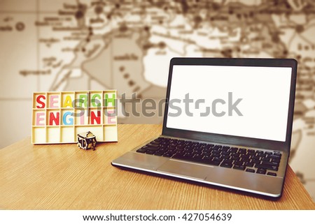 laptop and wooden word search engine with blur part of world map background