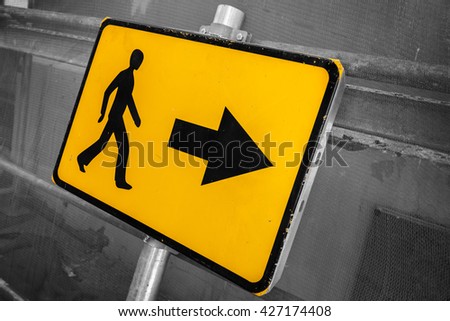 Pedestrians bypass direction. Yellow road sign on construction site fence