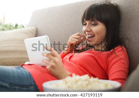 Attractive woman relaxing on the couch at home, she is watching videos online and eating popcorn, movies streaming concept
