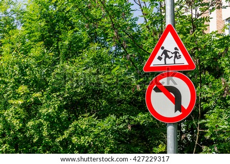 Traffic signs indicating to pay attention at kids that are crossing the street and it forbids turning left