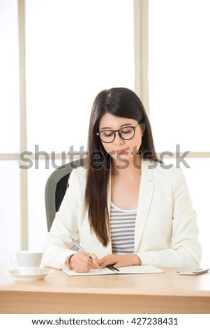 Young Asia businesswoman smiling and writing at desk in office
