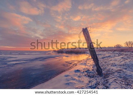 Fence post by a frozen lake in the sunrise