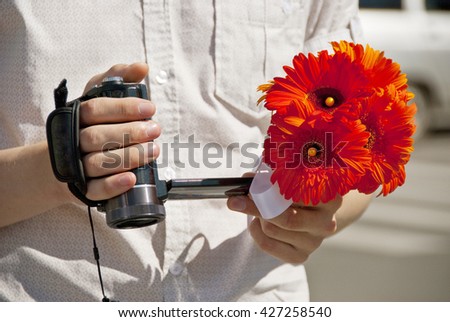 a video camera and a bouquet of red gerberas in the hands of man