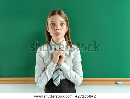 Cute schoolgirl near blackboard with folded hands in anticipation of something. Photo of teen school girl, creative concept with Back to school theme