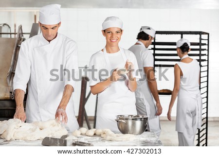 Female Baker Kneading Dough With Colleague In Bakery