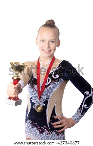 Portrait of beautiful happy smiling fit gymnast or skater young woman in sportswear dress posing with golden cup and first place medal, focus on the goblet, studio, isolated, white background