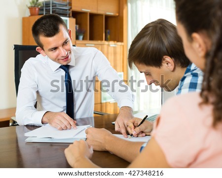 Smiling consultant explaining young couple details of mortgage in office 
